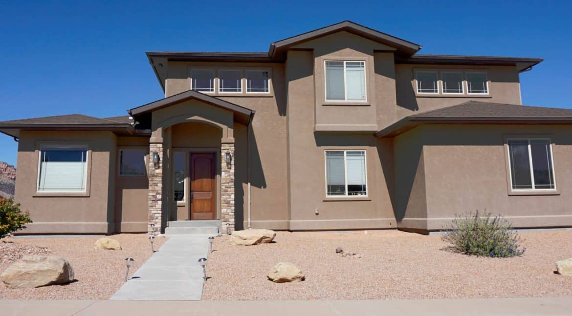 Bright, spacious two-story house with contemporary design, large windows, and inviting entrance, set against a scenic desert landscape. Perfect for luxury real estate investment and family living.