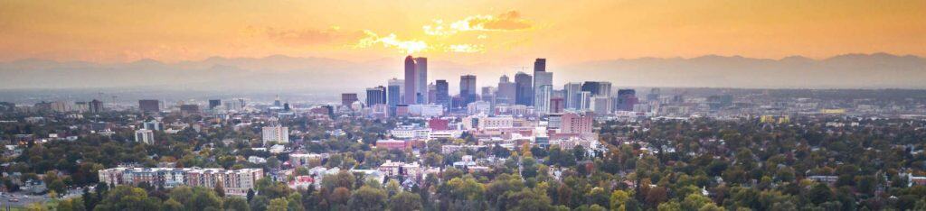 Panoramic view of Denver cityscape during sunset, highlighting the vibrant real estate market and scenic mountain surroundings.