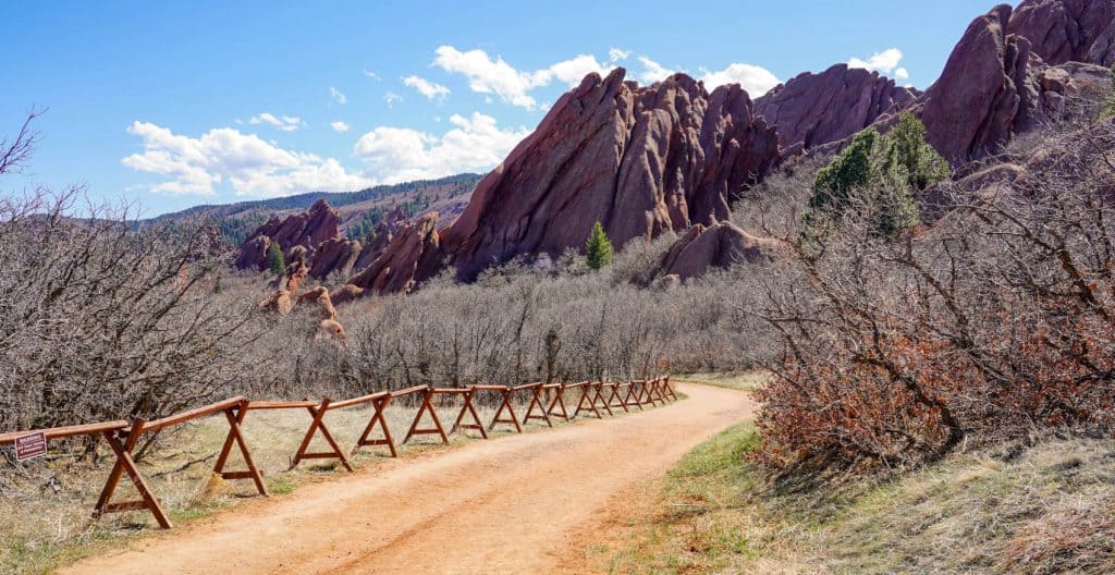 Stunning rocky mountain landscape with rugged red cliffs, a dirt trail, and sparse vegetation under a bright blue sky, ideal for outdoor adventure and scenic real estate locations.